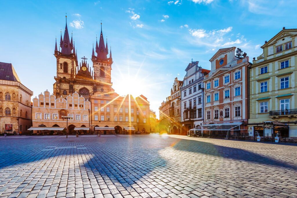 Sunrise illuminates Prague's Old Town Square, highlighting the Gothic spires of Tyn Church and the colorful facades of surrounding Baroque buildings.
