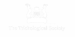 A monochrome logo featuring a crest with three stylized human figures, two of whom are lifting their arms, atop a banner that reads "The Trichological Society for Hair Implant.