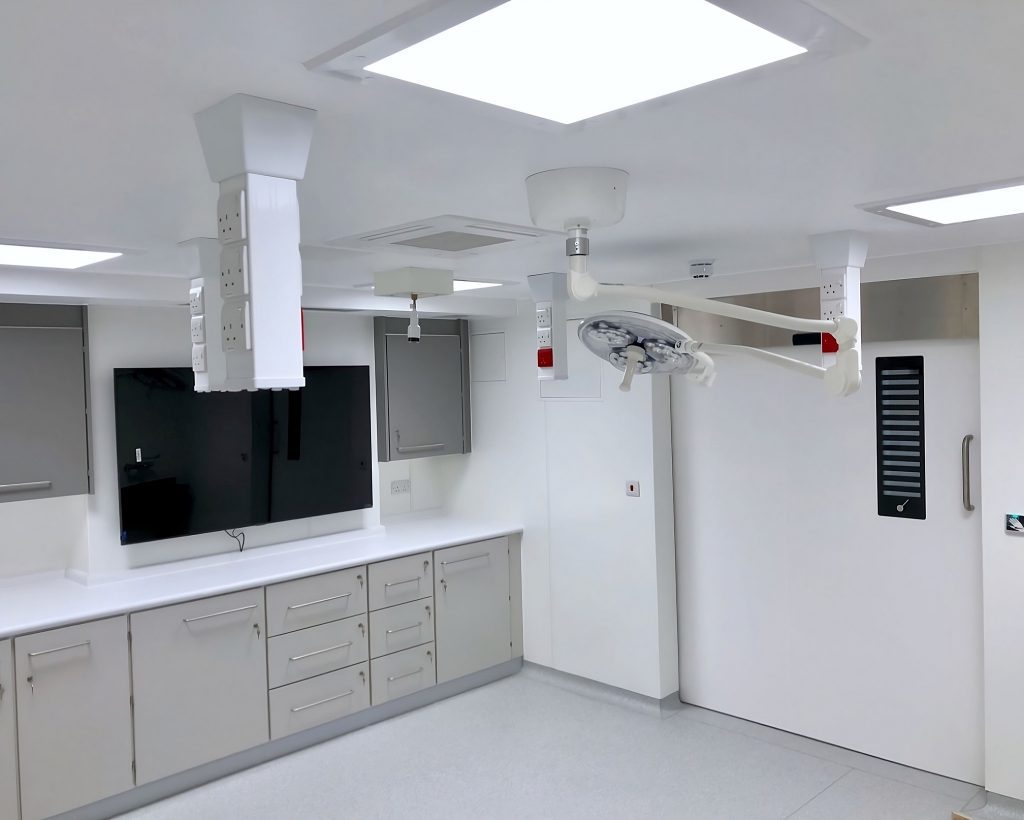 A modern, clean hospital surgical room specialized for hair replacement surgery, with white cabinetry and countertops, overhead surgical lights, and various medical equipment.